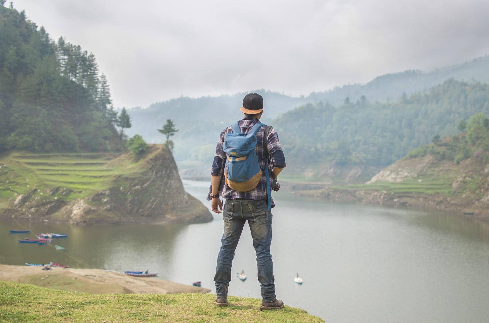 person in blue denim pants carrying blue backpack in front of body of water during daytime